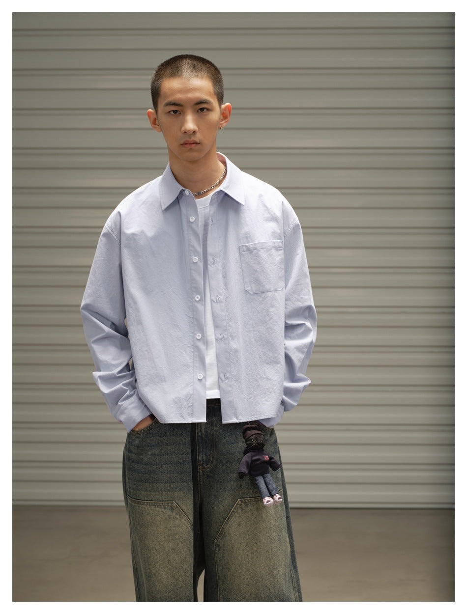 Front view of a model wearing a pale blue button-up shirt over a white tee, with a chest pocket and dark denim shorts.