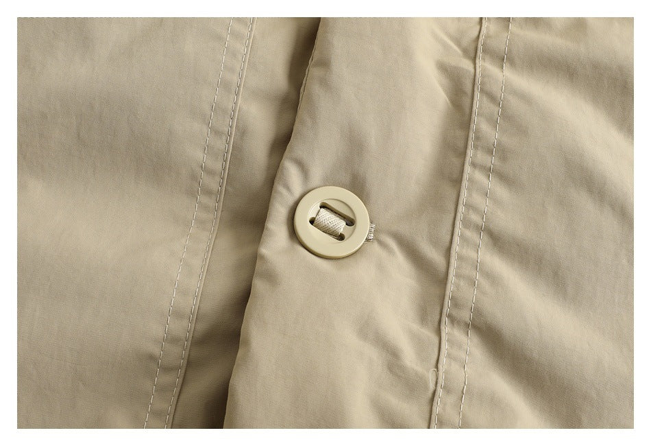 Close-up of a round beige button fastening the jacket’s stitched front placket.