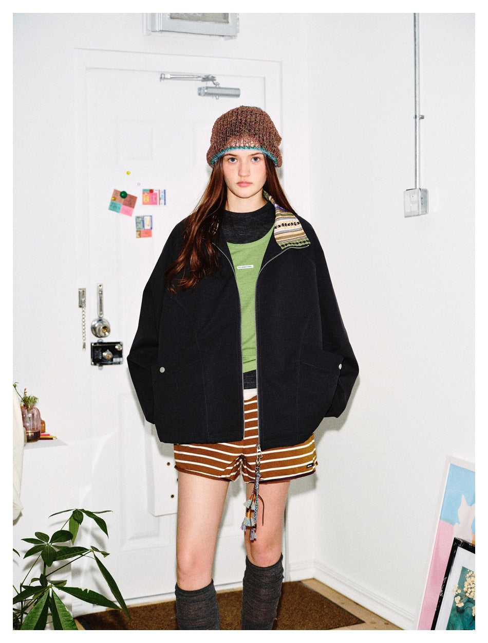 Model standing in a black zip jacket with striped collar, green top, striped shorts and knit beanie