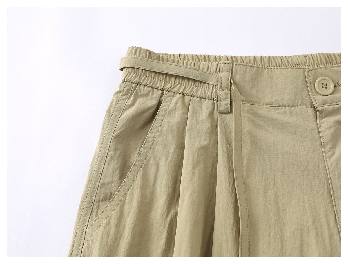 Close-up of beige shorts showing a front pleat, side pocket seam, belt loop and buttoned waistband.