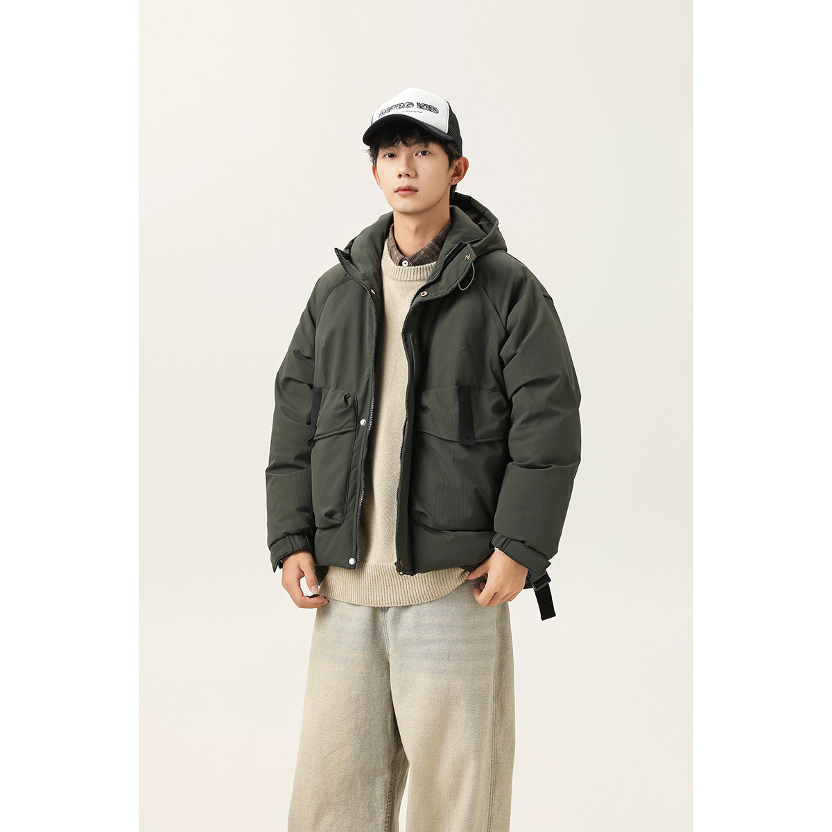 Front view of a model wearing a dark olive hooded jacket with oversized flap pockets and black trim.