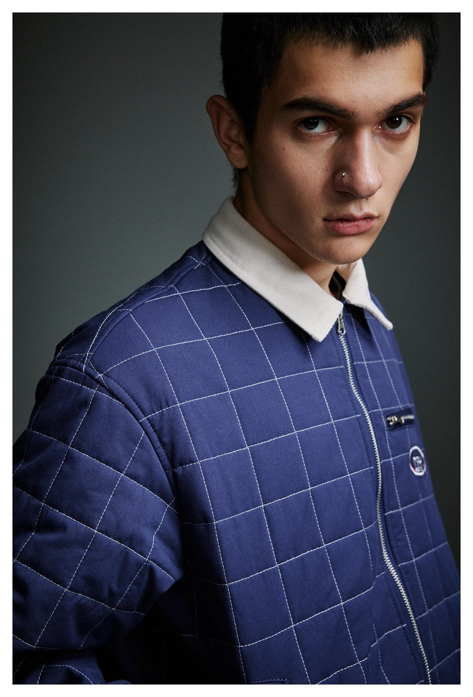 Close-up of a navy quilted jacket showing white grid stitching, cream collar, zipper and chest pocket.