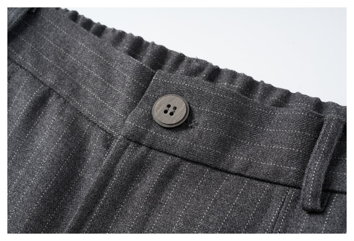 Detail of the dark button, gathered waistband and pinstripe fabric on charcoal trousers.