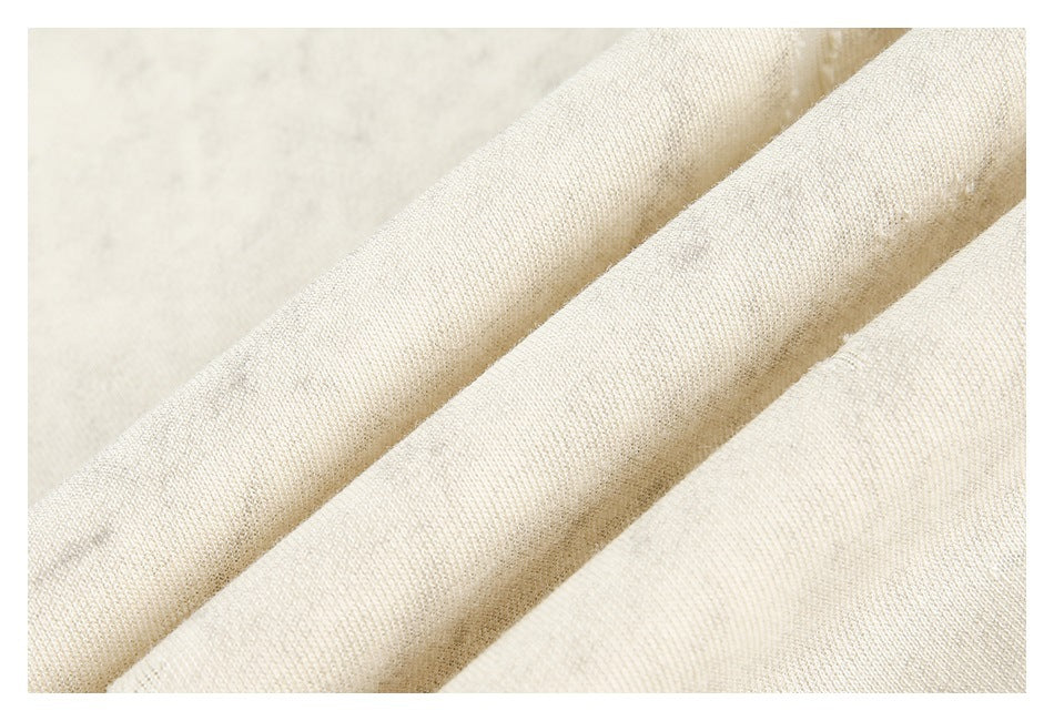 Close-up of cream-colored fabric folded into soft diagonal ridges, showing its fine textured weave.
