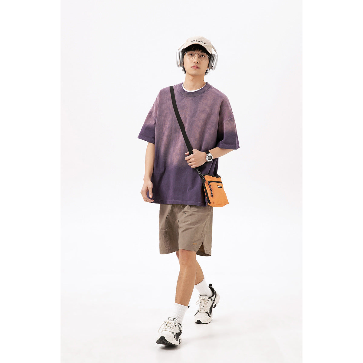 Model wearing taupe shorts and an oversized purple T-shirt, with a cap, headphones, and orange crossbody bag.