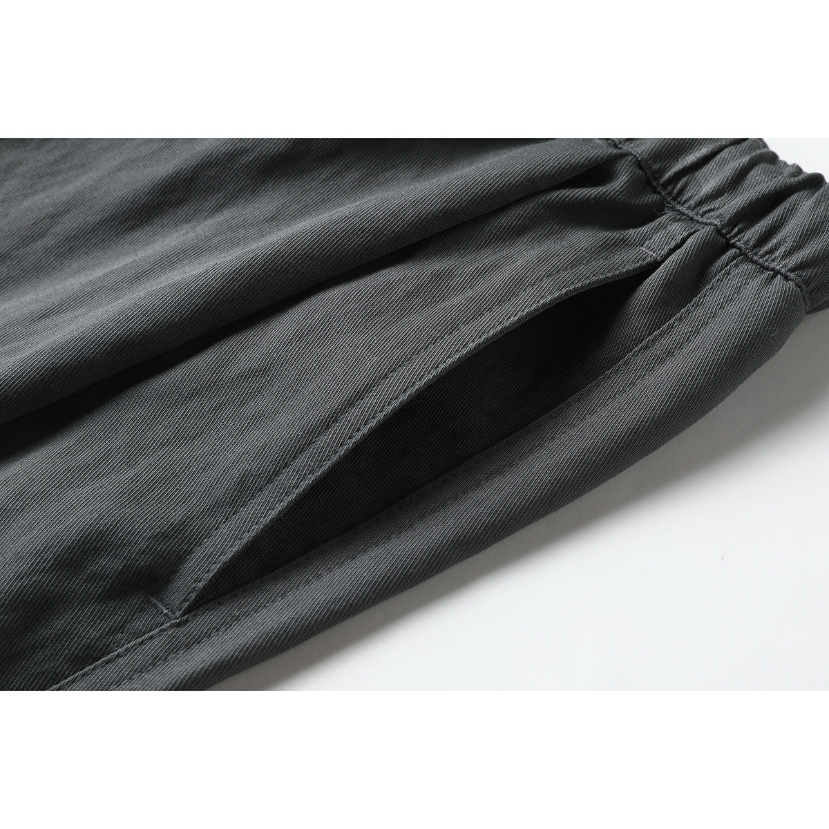 Close-up of charcoal gray trousers showing a deep side pocket opening and stitched fabric details.