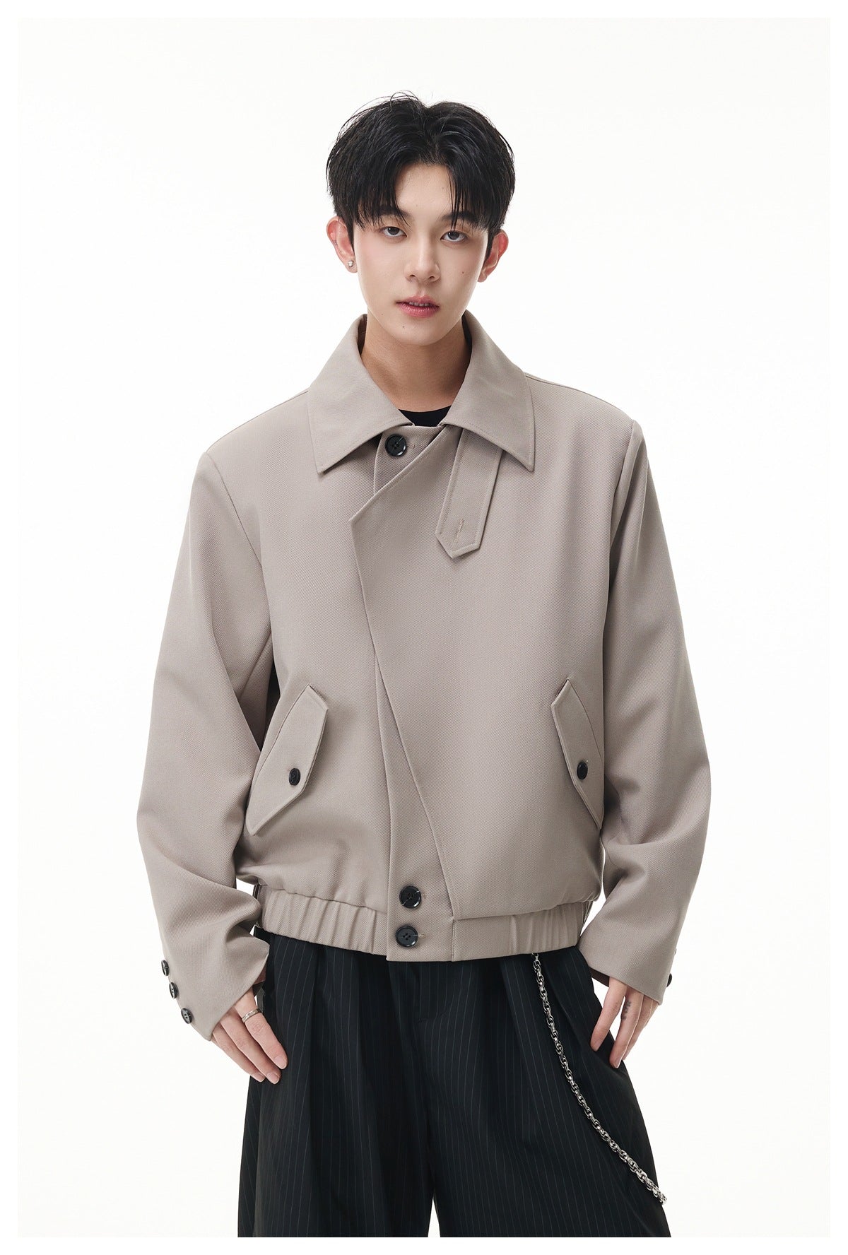 Front view of a model wearing a taupe jacket with a broad collar, asymmetric buttoned front and angled pockets.