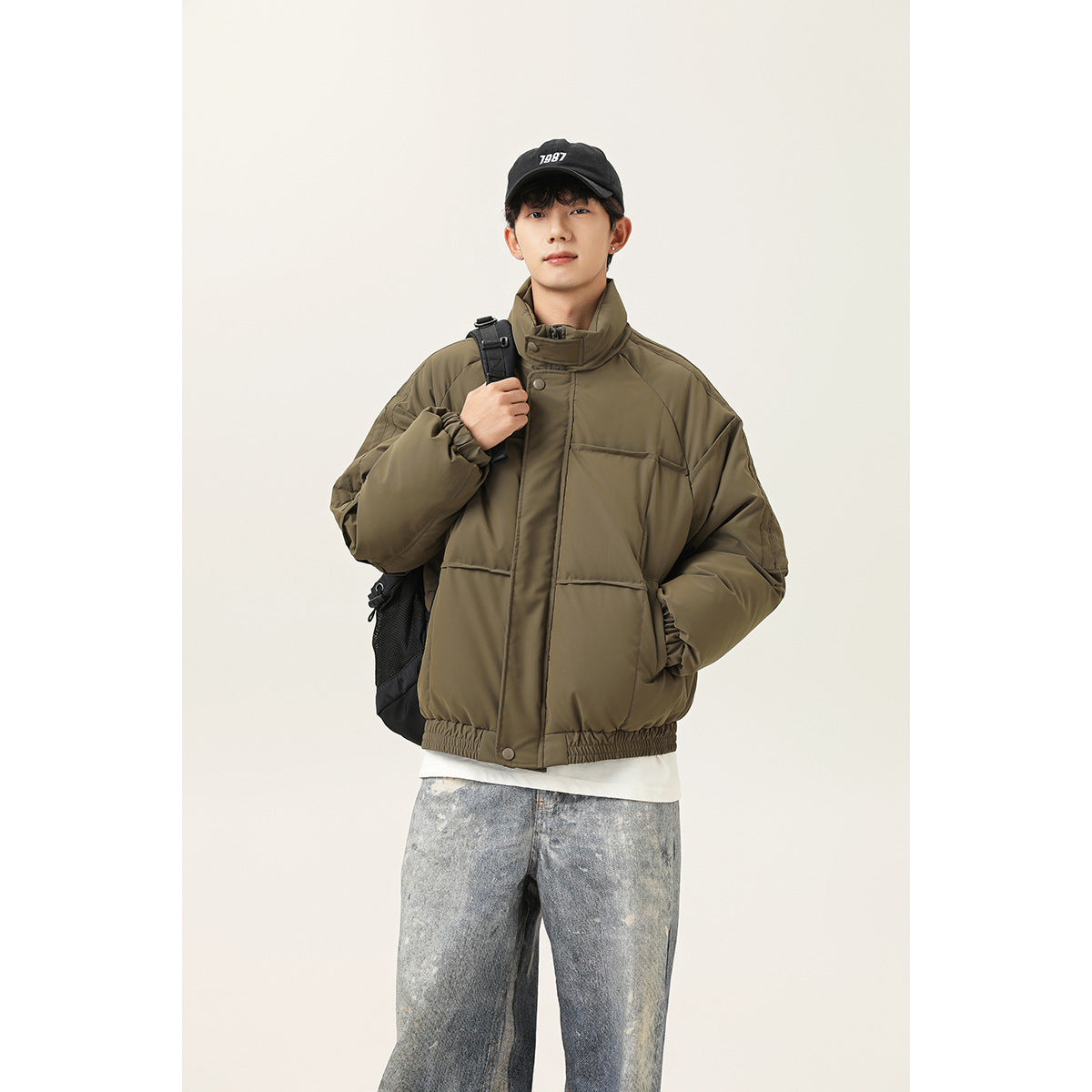 Man wearing an olive oversized jacket with a high collar, snap-front storm flap, and large patch pockets.