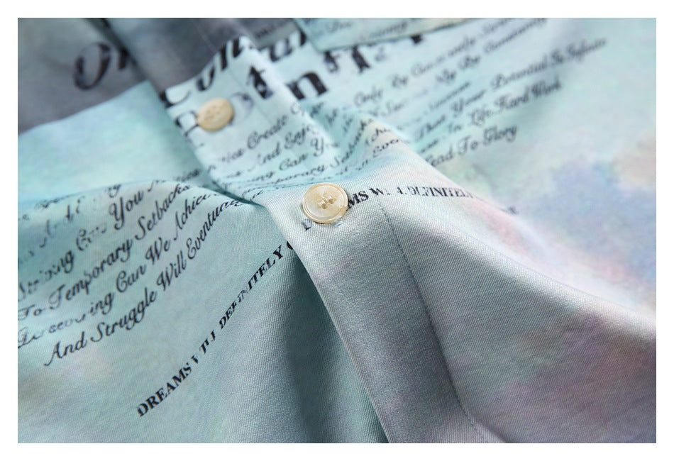 Close-up of the pale aqua shirt's button, placket, and cloudy pastel print with black lettering.