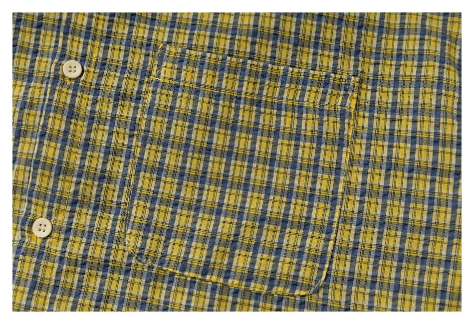 Close-up of the yellow and blue plaid shirt's chest pocket, stitching, and cream buttons.