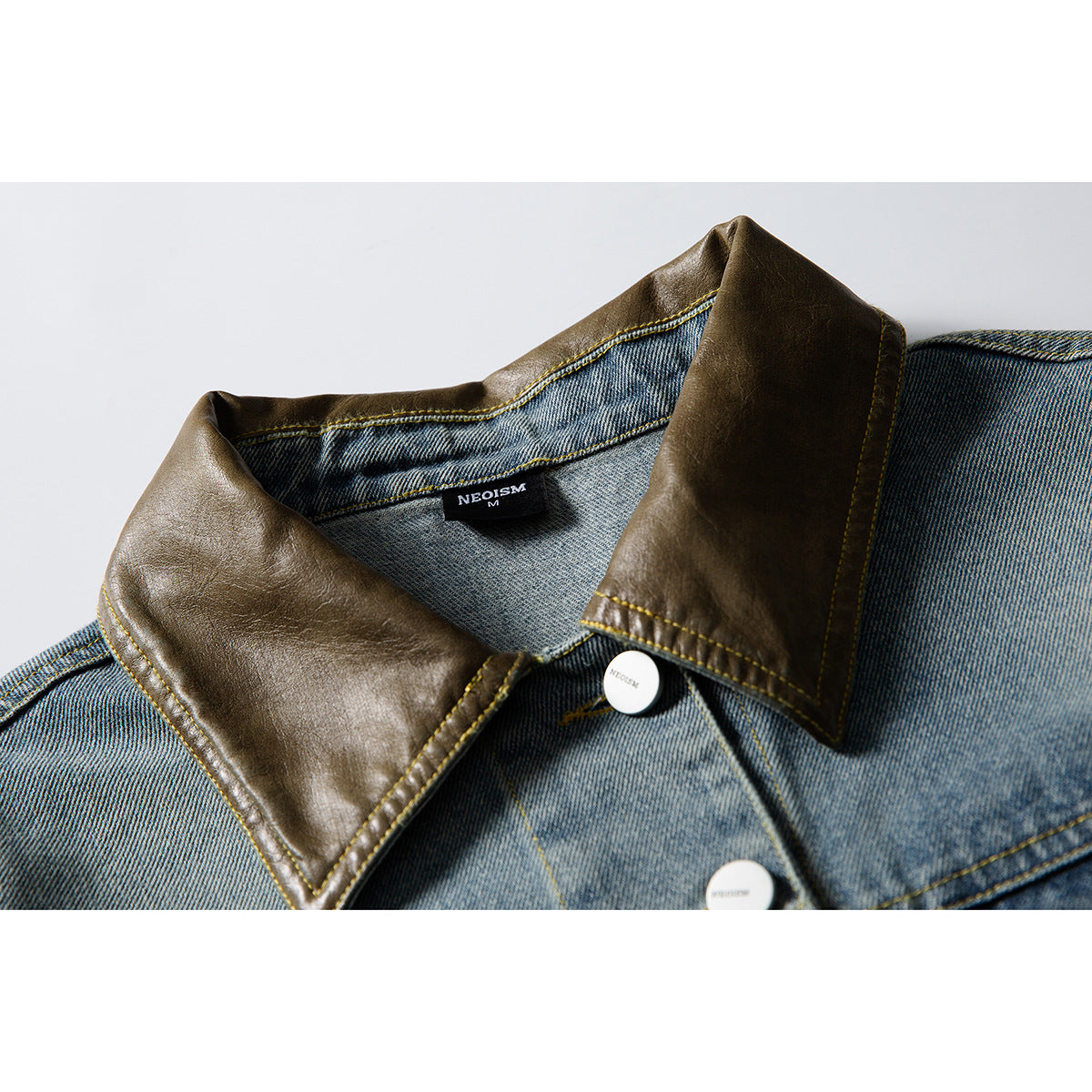 Close-up of a faded blue denim jacket with a dark brown collar, yellow stitching, and white buttons.