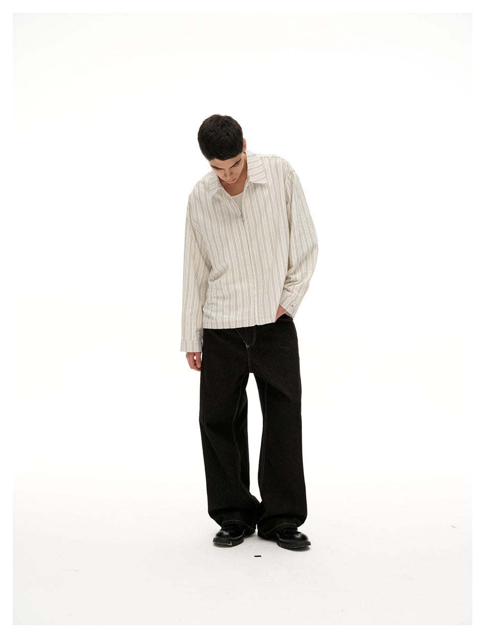 Model looks down in a cream shirt with fine vertical stripes and wide black trousers.