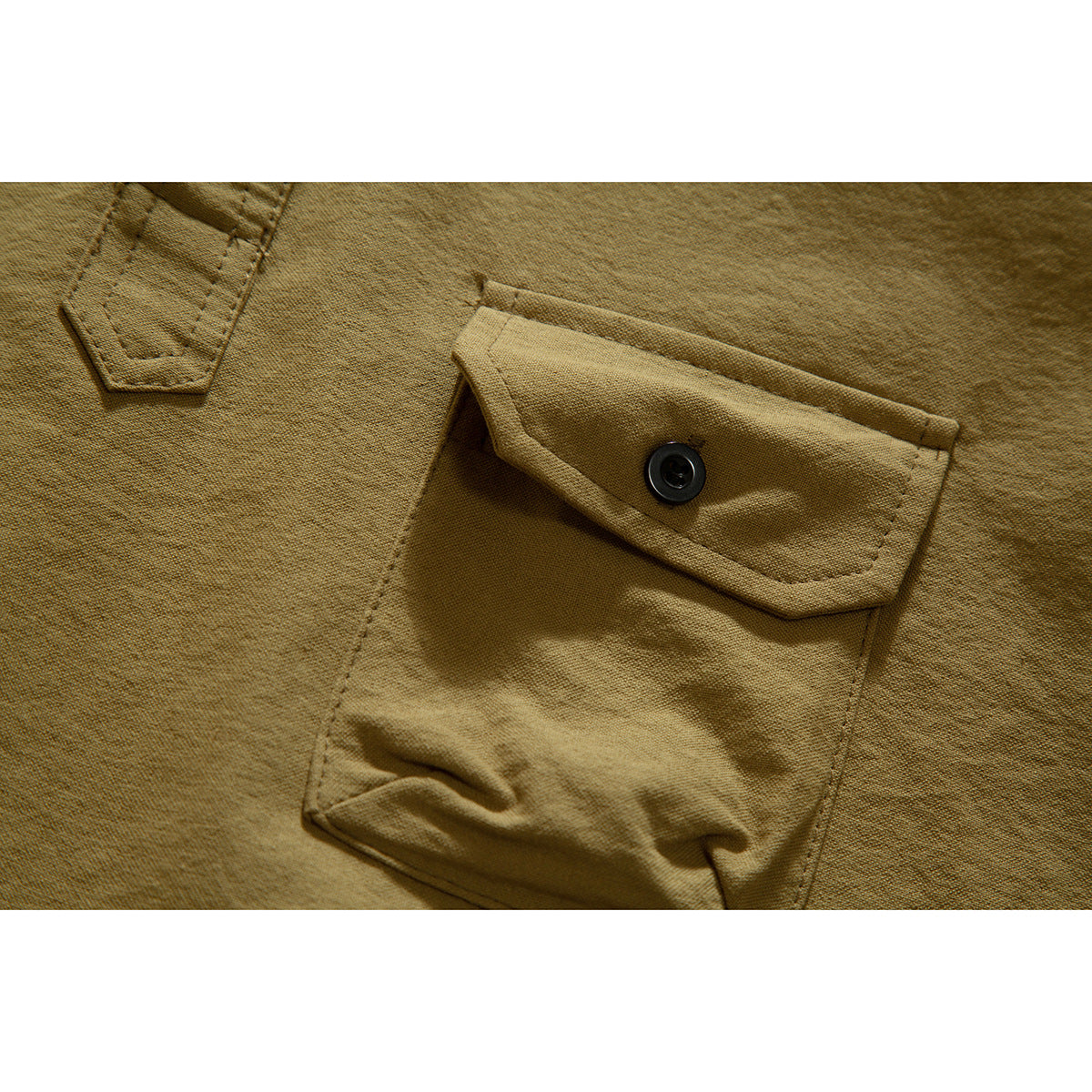 Close-up of a tan shirt's buttoned chest pocket and visible stitching.