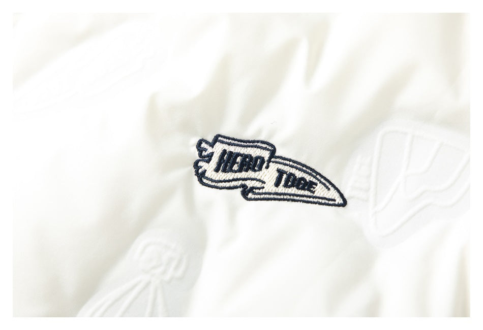 Close-up of an embroidered navy patch on the white jacket, surrounded by subtle raised motifs.