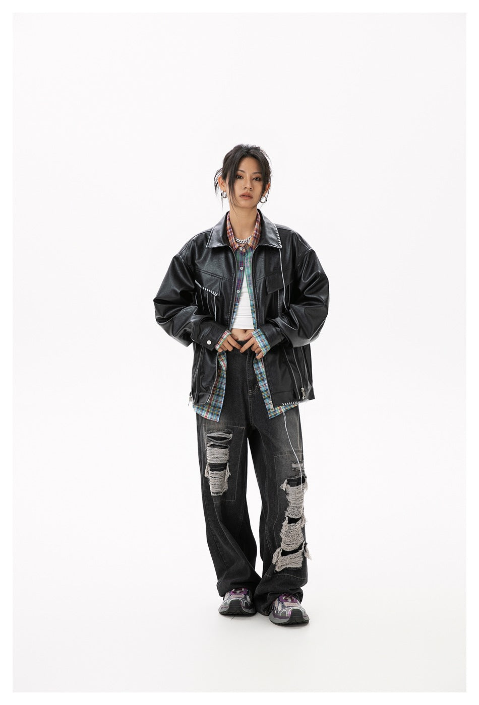 Front view of a model in a black jacket with white stitch details, plaid shirt, and loose distressed jeans.