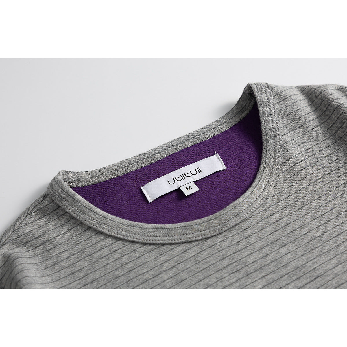 Close-up of a gray finely striped shirt's round neckline, showing purple inner facing and a sewn label.