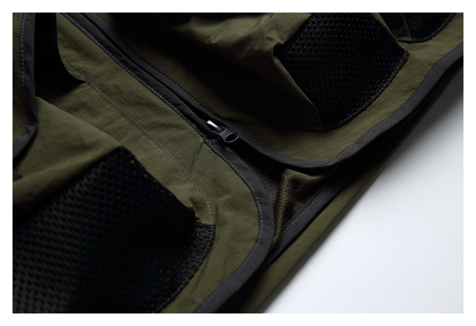 Close-up of olive-green fabric with a dark-trimmed zipper and black mesh pockets.