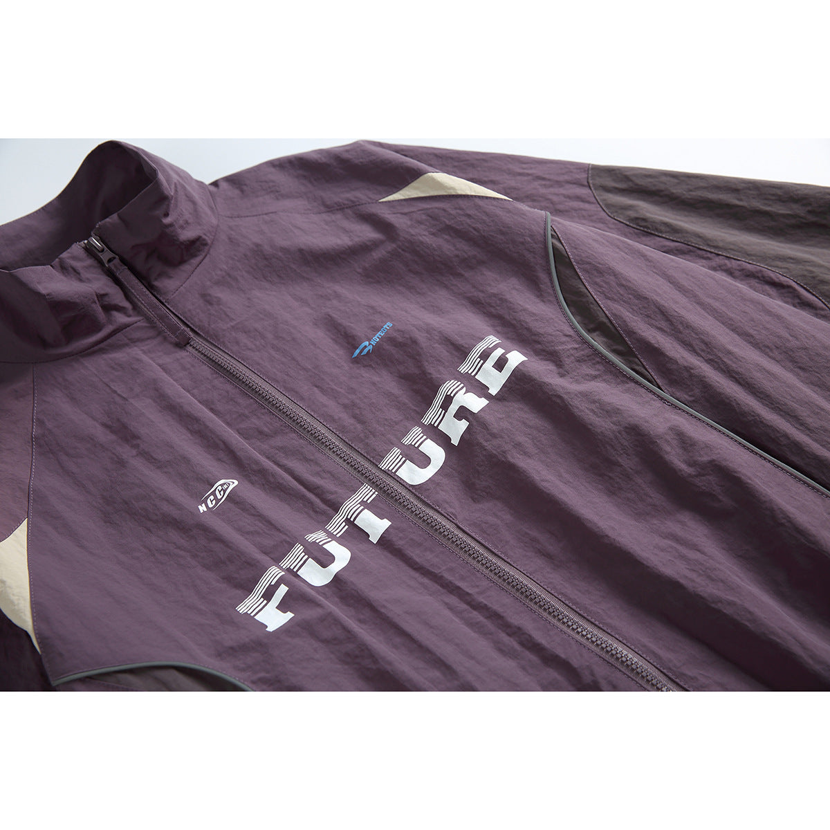 Close-up of a plum zip-up jacket front with a high collar, color-block panels, and large white FUTURE lettering.