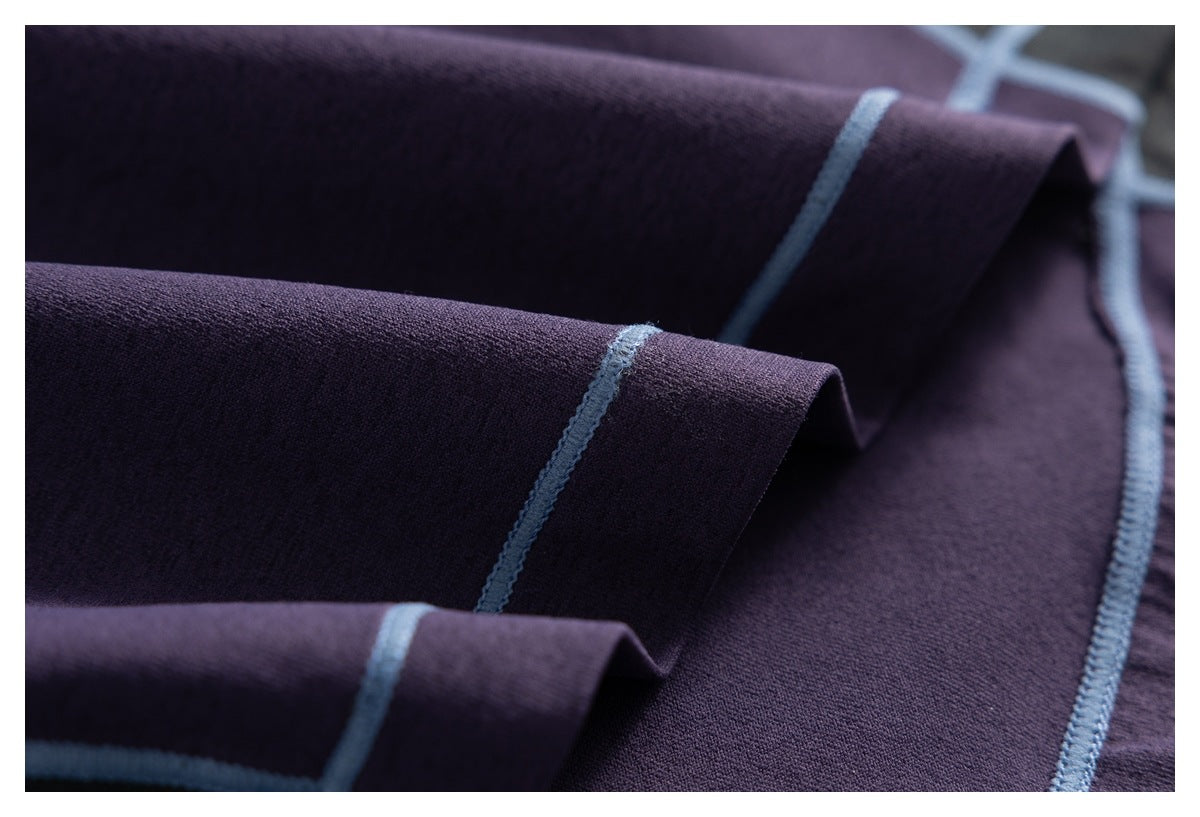 Close-up of dark purple fabric folds with pale blue overlocked seams.