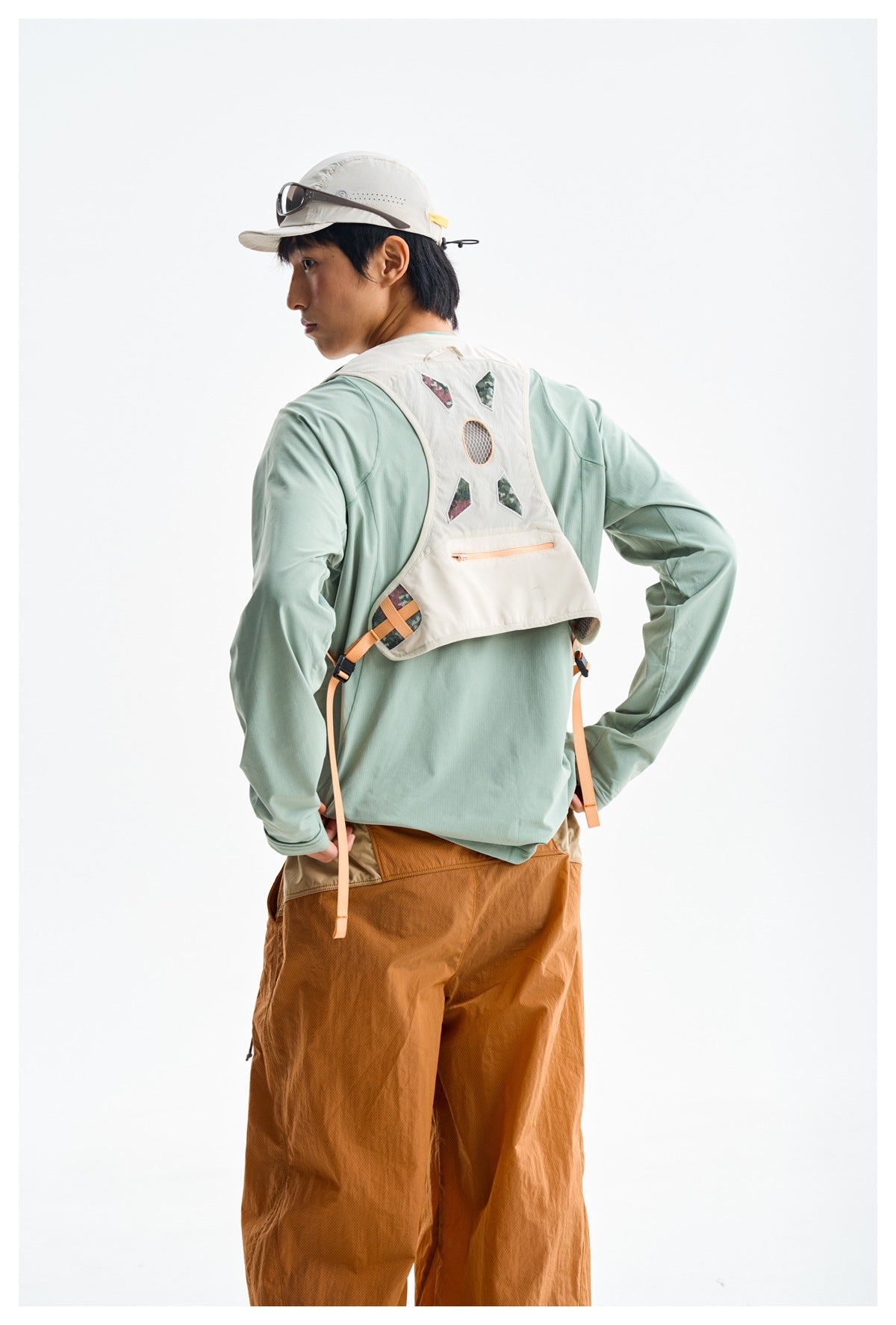 Back view of a man wearing a cream trail-running vest with patterned panels, a horizontal zipper pocket and orange adjustment
