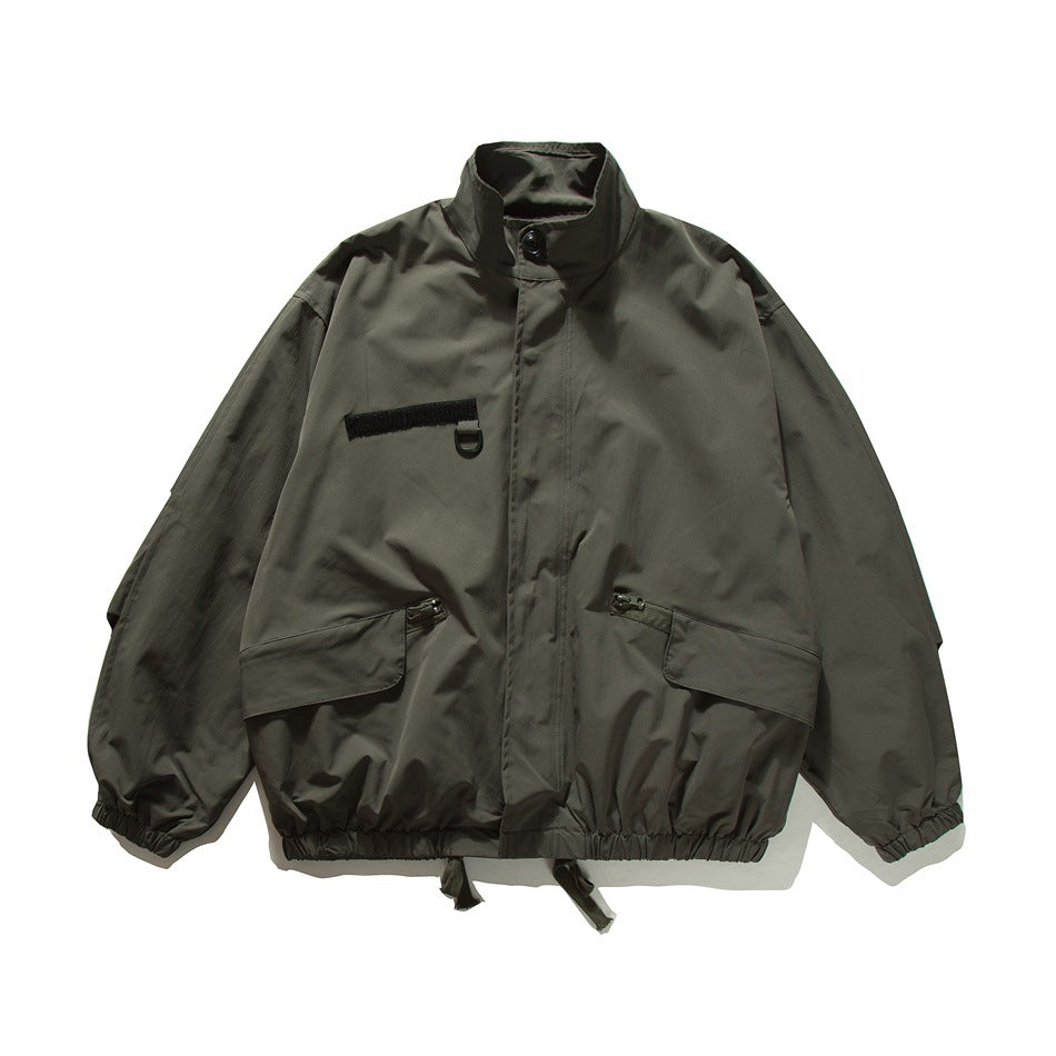 Dark gray stand-collar bomber-style jacket, flat front view with chest patch, flap pockets and elastic hem