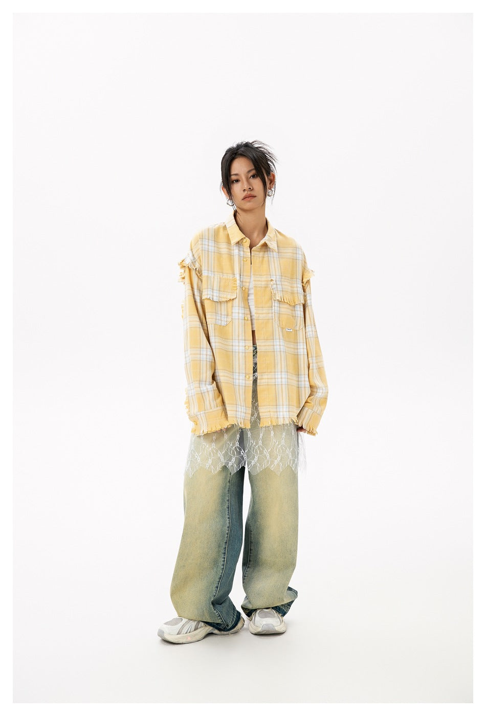 Full-length front view of a model wearing a yellow plaid shirt with frayed details, lace overlay, and wide-leg jeans.