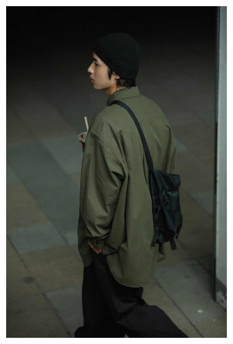 Rear three-quarter view of a model wearing an oversized olive-green shirt and black trousers.