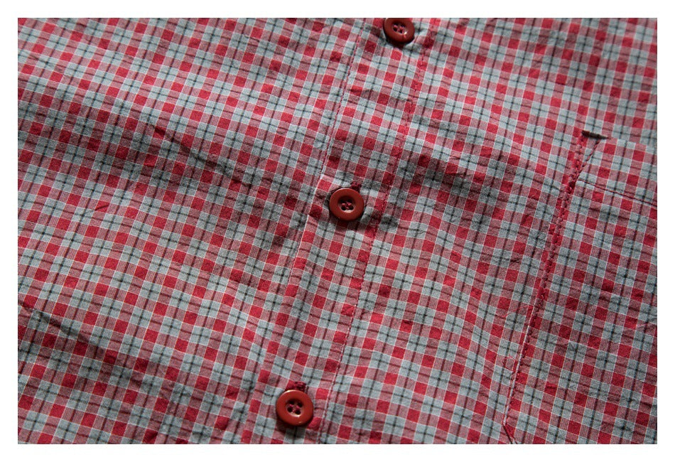 Close-up of a red, gray, and white plaid shirt front with red buttons and a chest pocket.