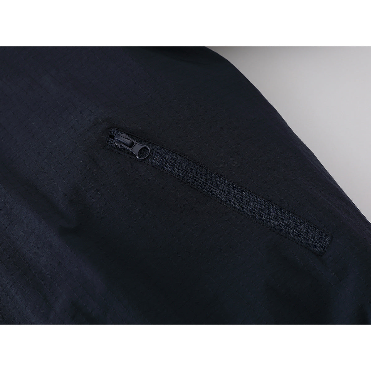 Close-up of a slanted zip pocket on dark navy textured jacket fabric.
