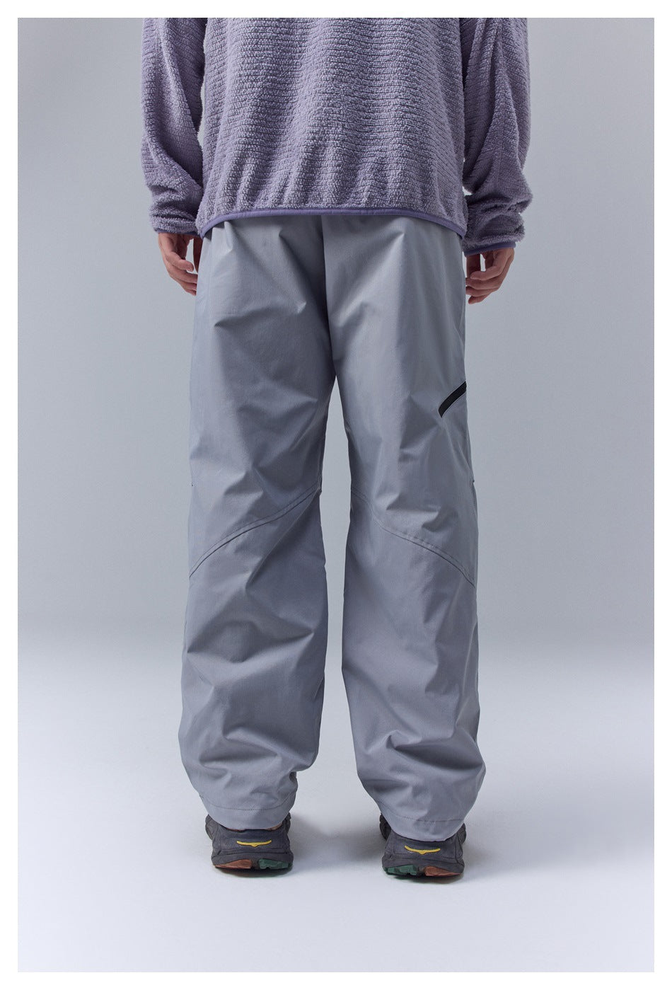 Back view of a person wearing loose gray pants with curved leg seams and a small black detail on one thigh.