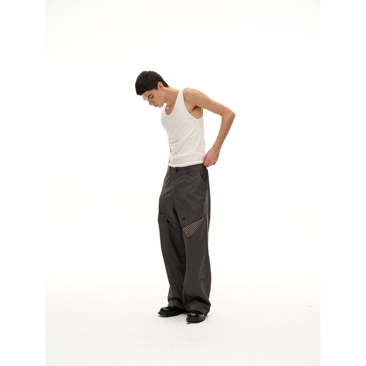 Model in a cream tank top and charcoal wide-leg trousers with a plaid pocket accent, shown at a side angle.
