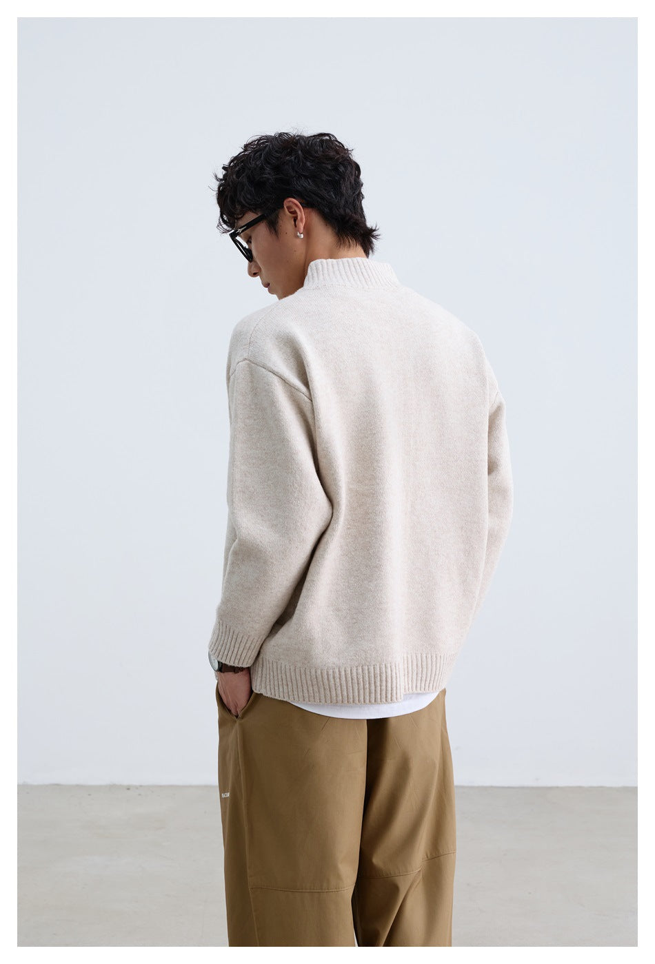 Rear view of a man wearing an ivory knit sweater with a ribbed collar and hem.