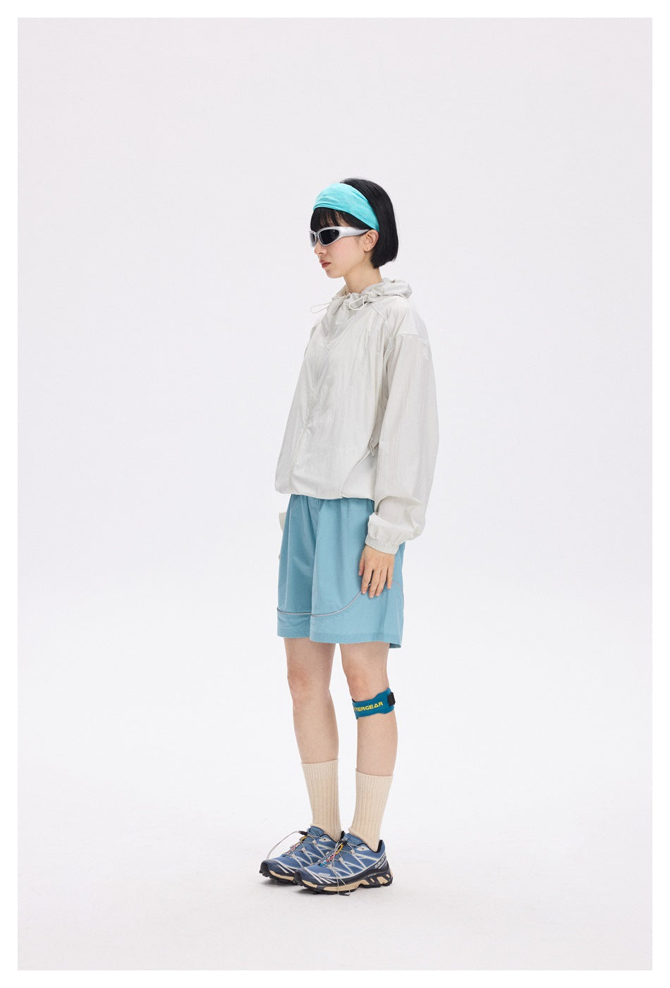 Model in profile wearing an off-white hooded jacket and light blue shorts with outdoor accessories.