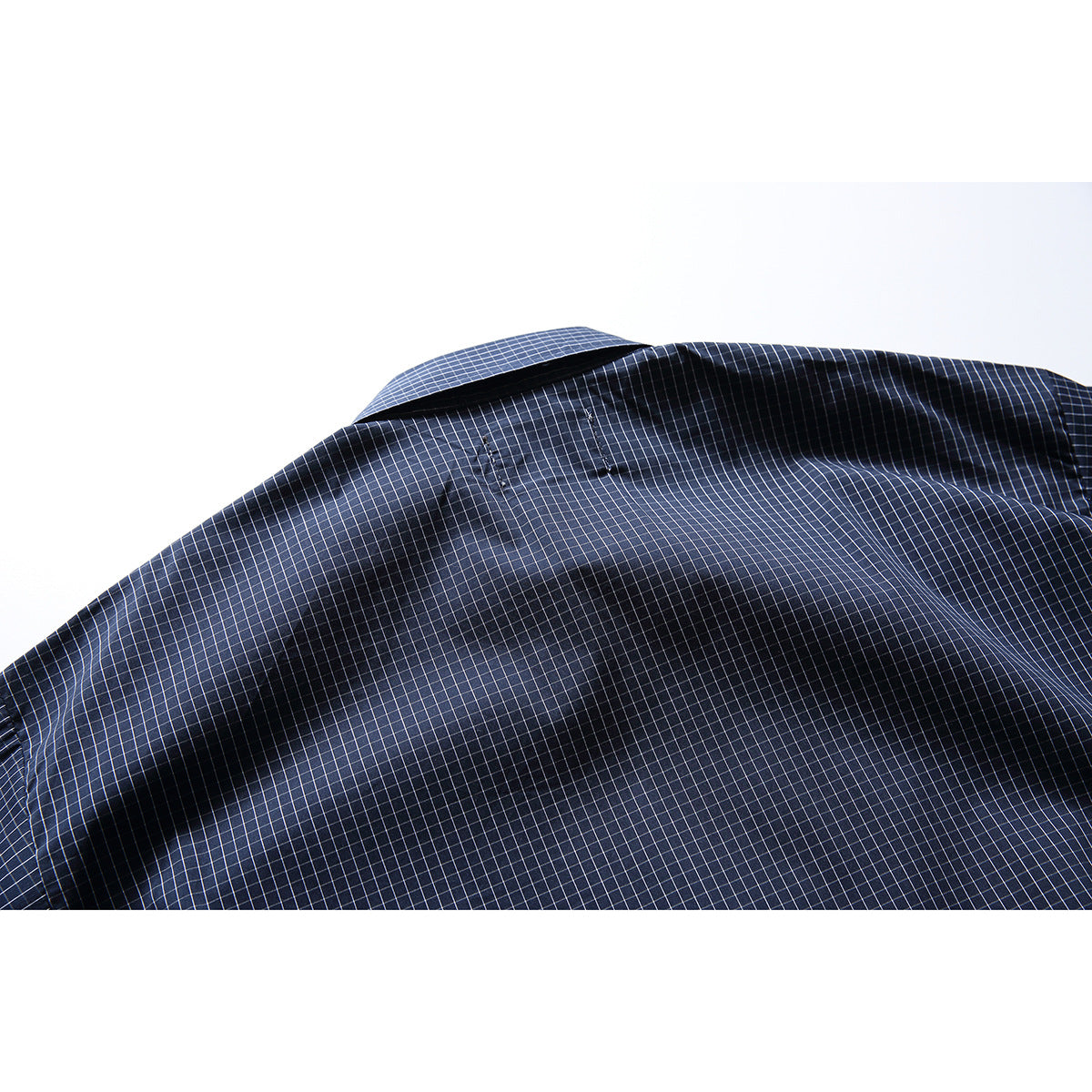 Close-up of the back yoke and collar of a navy shirt with a fine white grid check.
