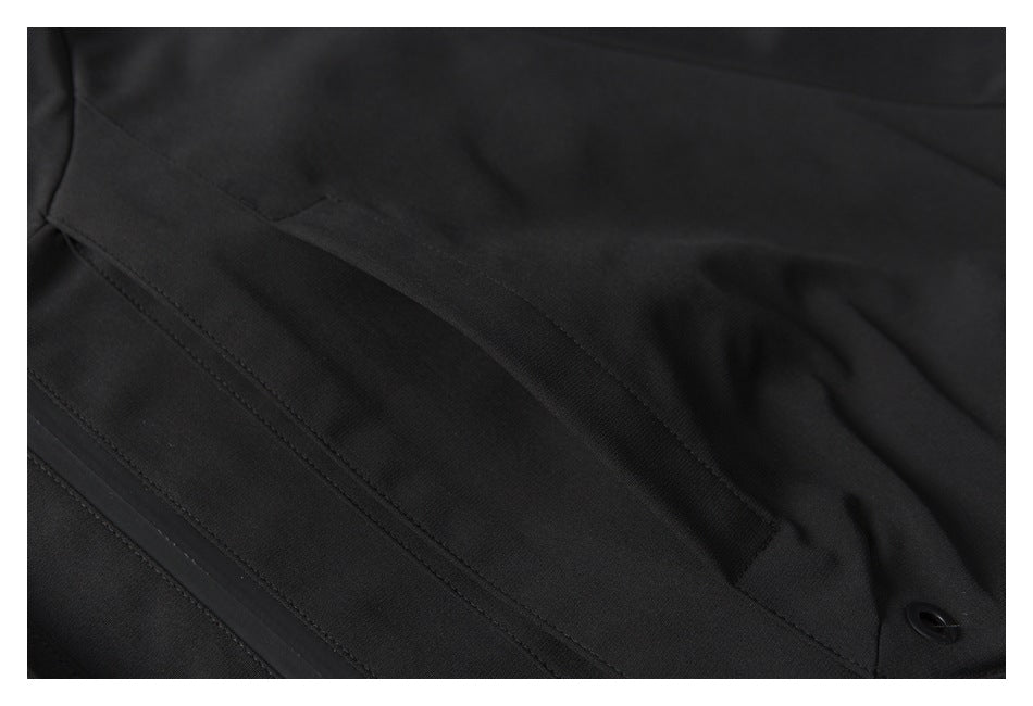 Close-up of black jacket fabric with stitched panels, a narrow flap, and a small eyelet.