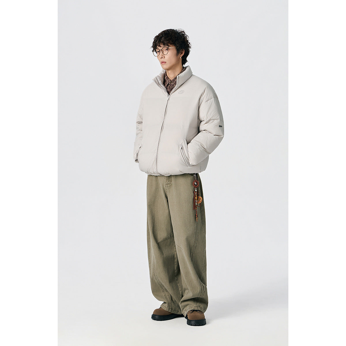 Model wearing a light gray padded jacket with a stand collar and zip pockets, styled with wide olive trousers.
