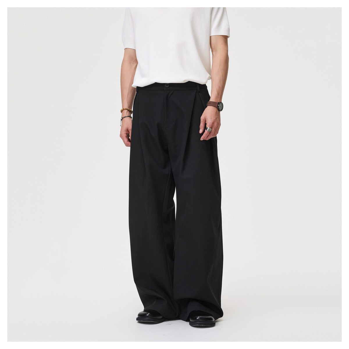 Model wearing black pleated wide-leg trousers, shown from the front against a light background.