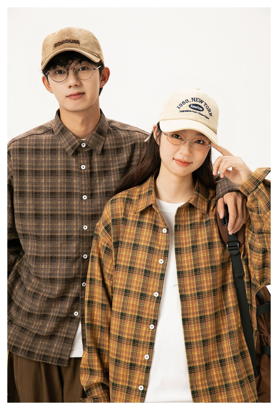 Close view of two models wearing brown and mustard plaid button-up shirts over white tops.