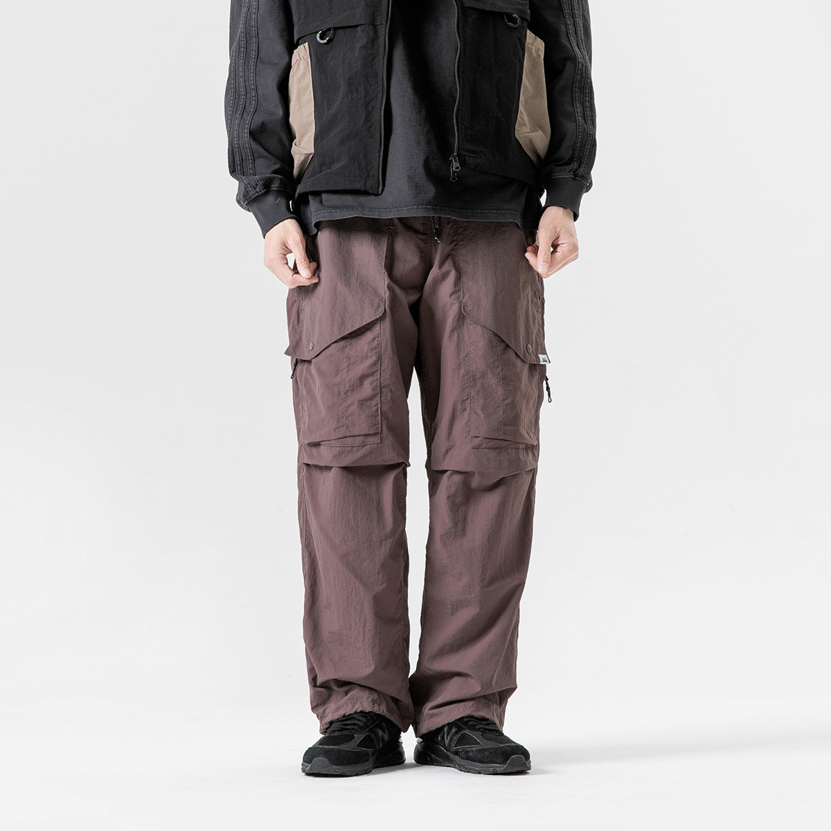 Front view of a model wearing loose mauve-brown cargo pants with large flap pockets and layered knee panels.