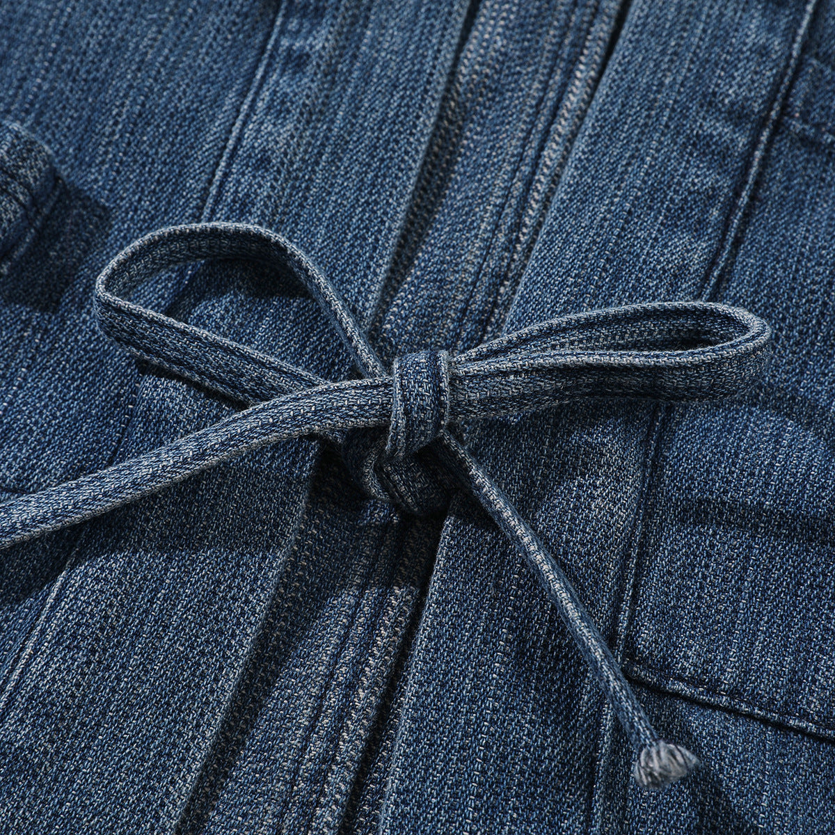 Close-up of a dark blue denim jacket’s matching tie belt knotted at the waist.