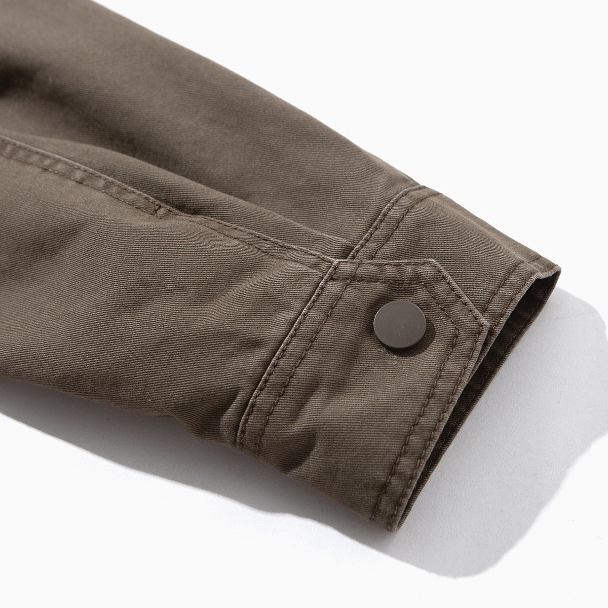 Close-up of a taupe jacket sleeve cuff with a dark button and stitched seams.