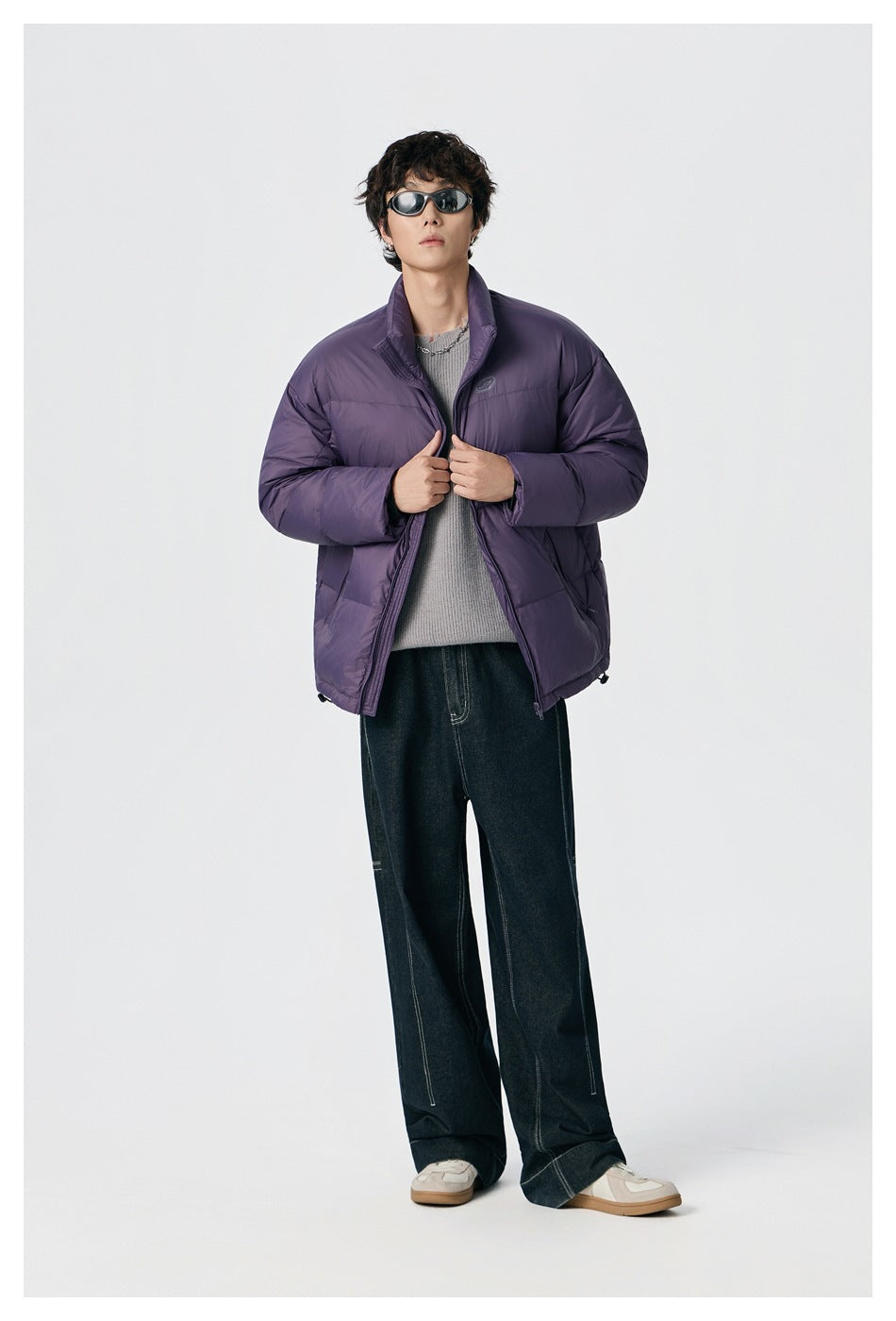 Model wearing an open purple puffer jacket with a high collar, quilted panels, and side pockets.