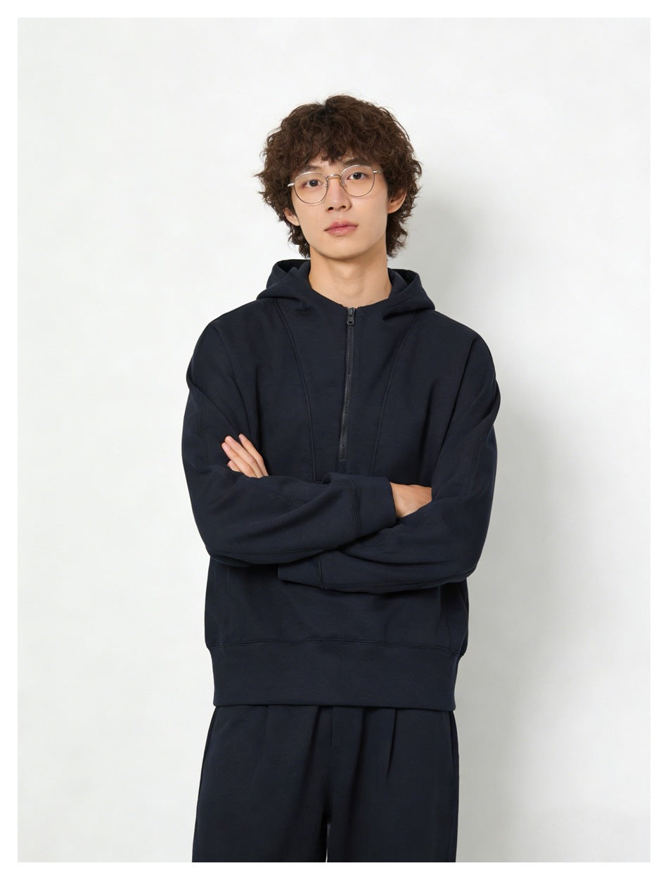 Model with crossed arms wearing navy half-zip hoodie, close-up of chest panel, zipper and ribbed cuffs