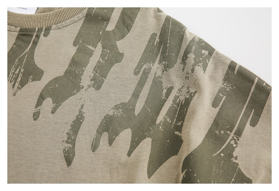 Close-up of the abstract dark olive print and fabric on a khaki T-shirt shoulder.