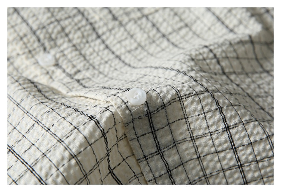 Close-up of a white button on the off-white shirt's black windowpane-check fabric.