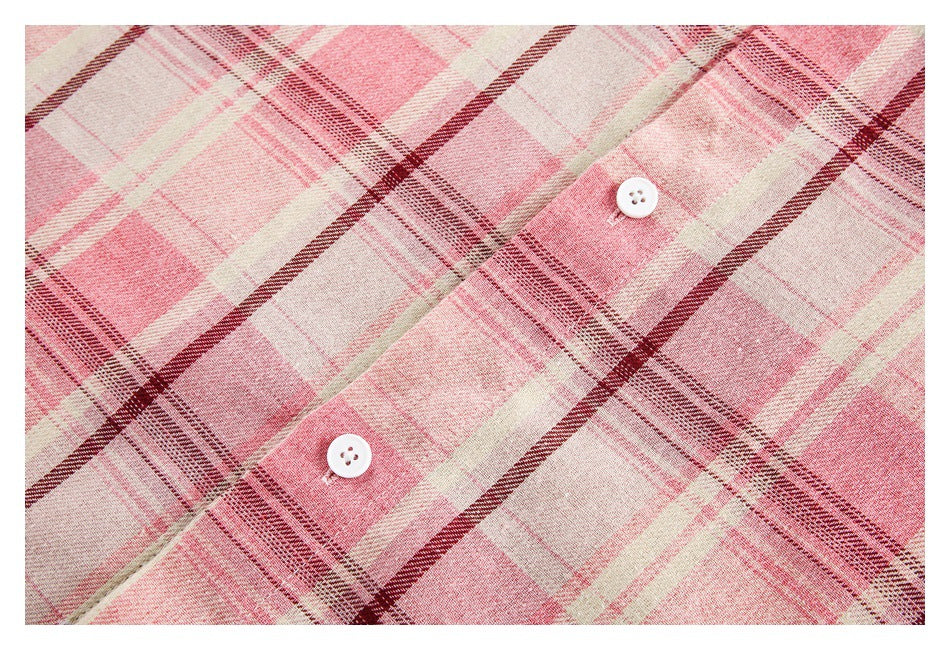 Close-up of two white buttons on a pink, cream, and burgundy plaid shirt placket.