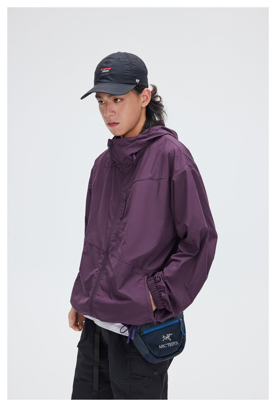 Closer view of a model in a plum hooded jacket, showing its front zip and a blue crossbody bag.