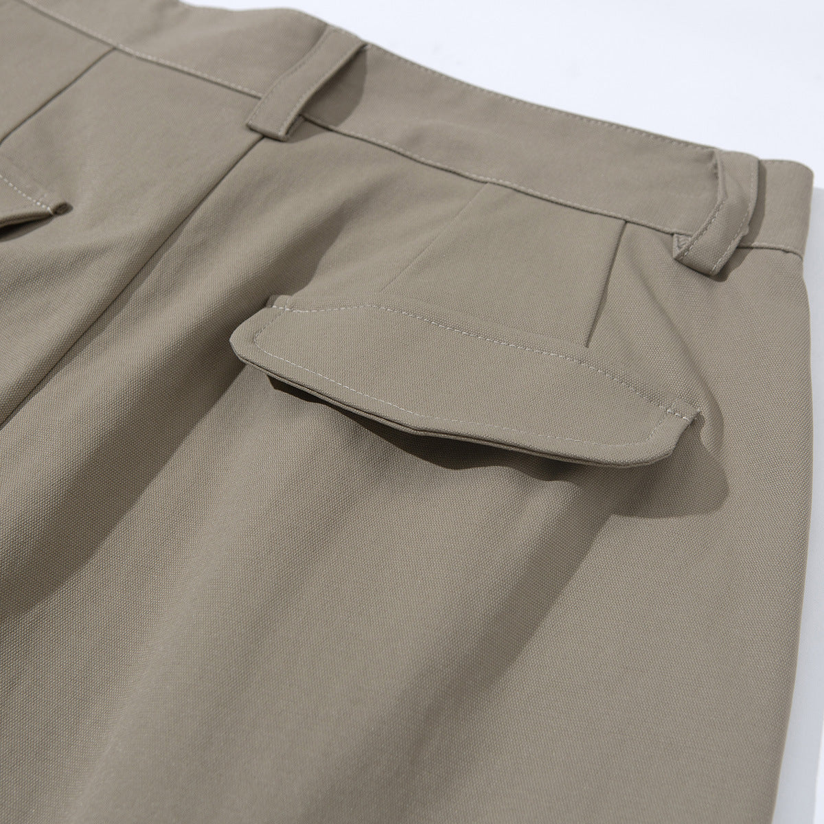 Close-up of taupe tailored shorts showing a flap pocket on the back and waistband belt loops.