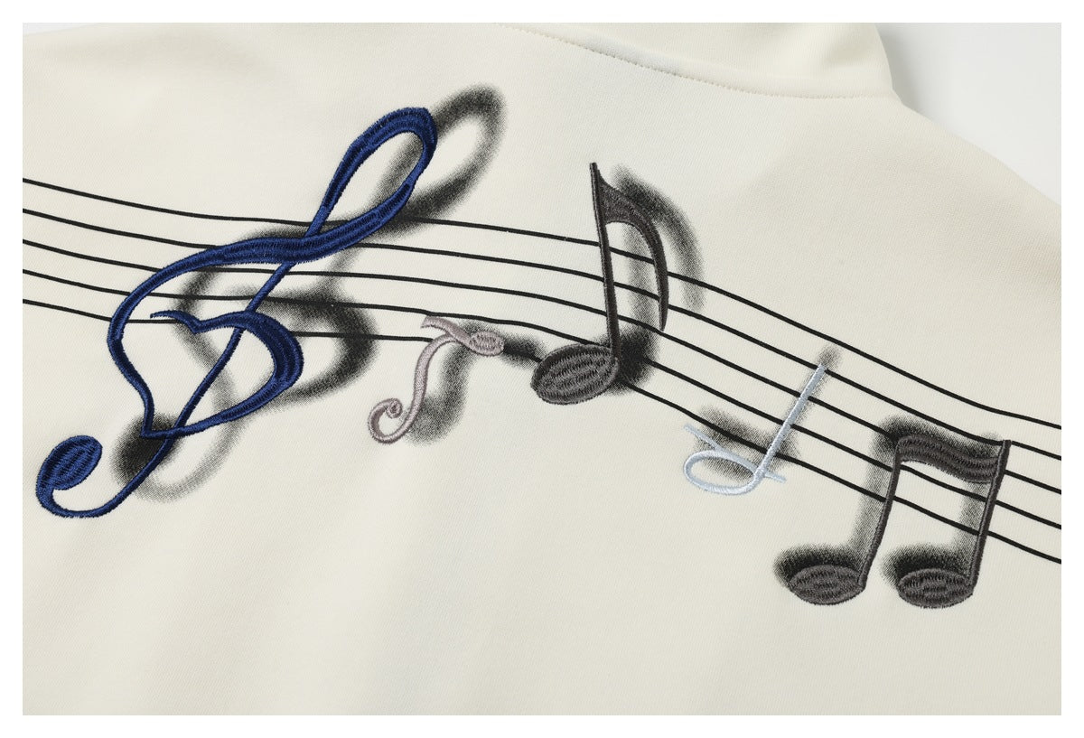 Close-up of colorful embroidered musical notes over a black staff on ivory fabric.