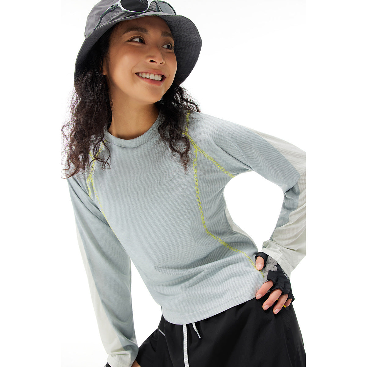Woman wearing a pale blue-gray long-sleeve athletic top with yellow seam accents and contrasting light sleeves.